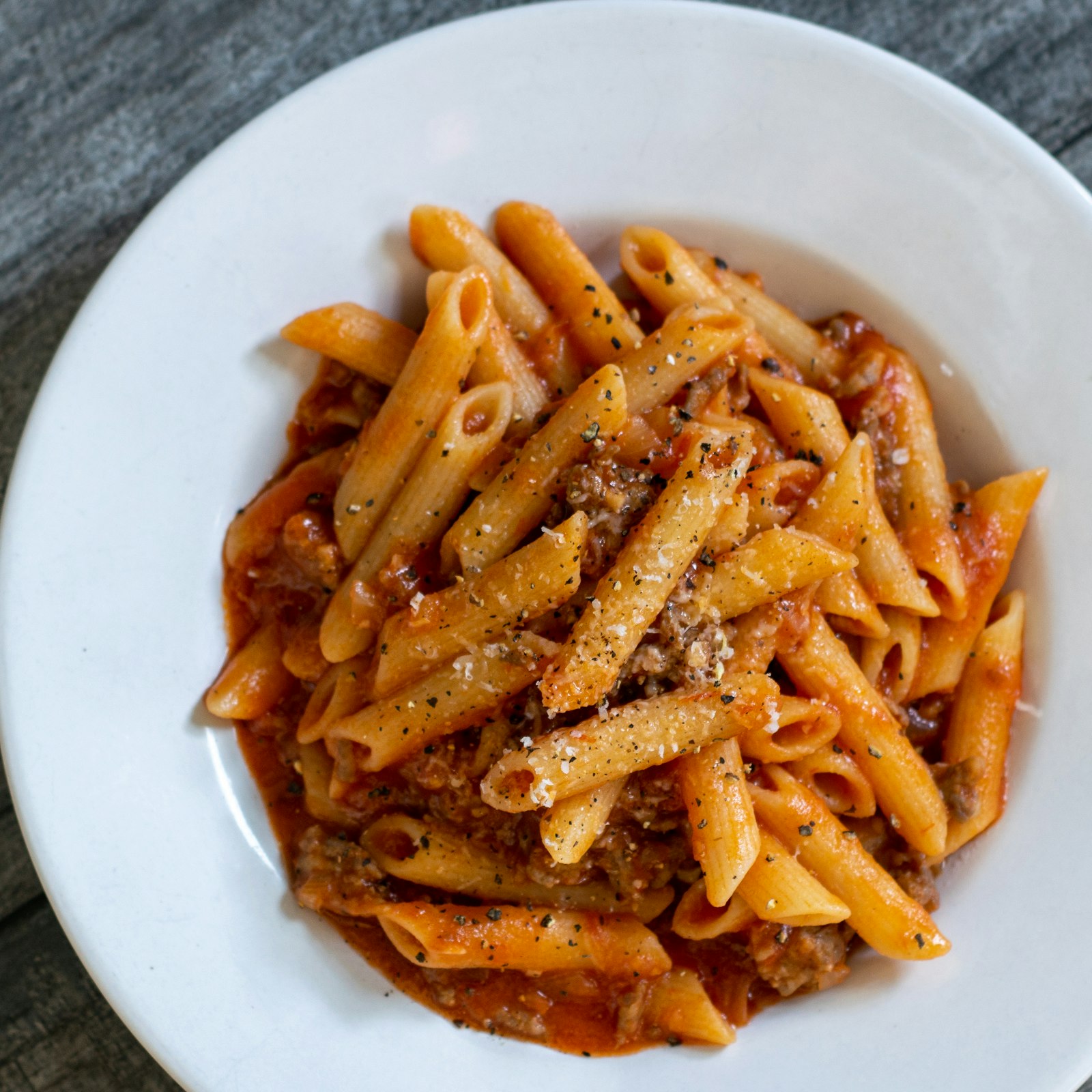 Bowl of rigatoni coated in roasted tomato sauce with spoonfuls of ricotta and torn basil